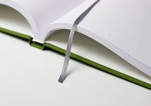Hardcover book in green linen, lying open, with bookmark ribbon